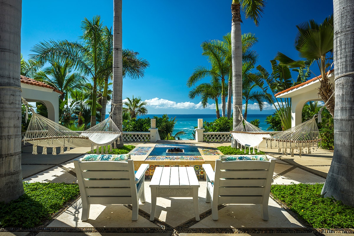 Fire table lounge with hammocks framed by palms and the ocean at Casa Edwards, Palmilla, Los Cabos