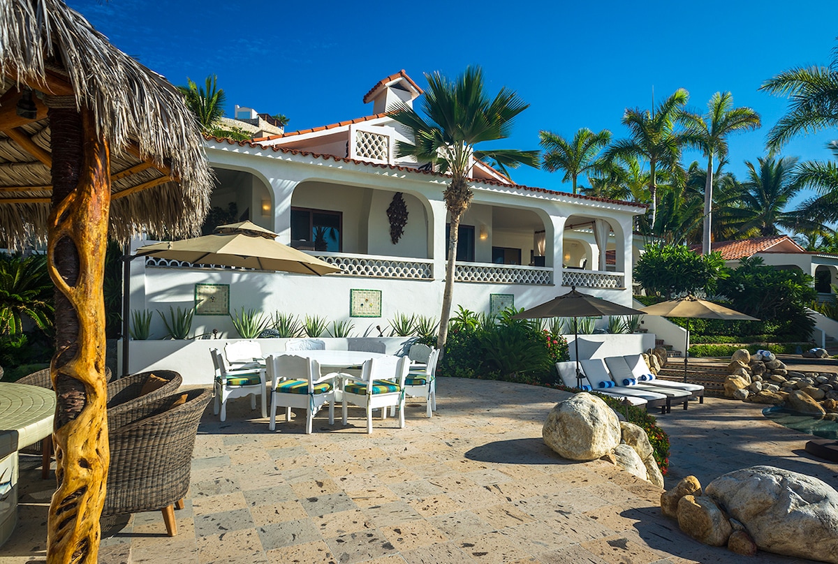 Shaded outdoor dining table under the palapa with the main house behind at Casa Edwards, Palmilla