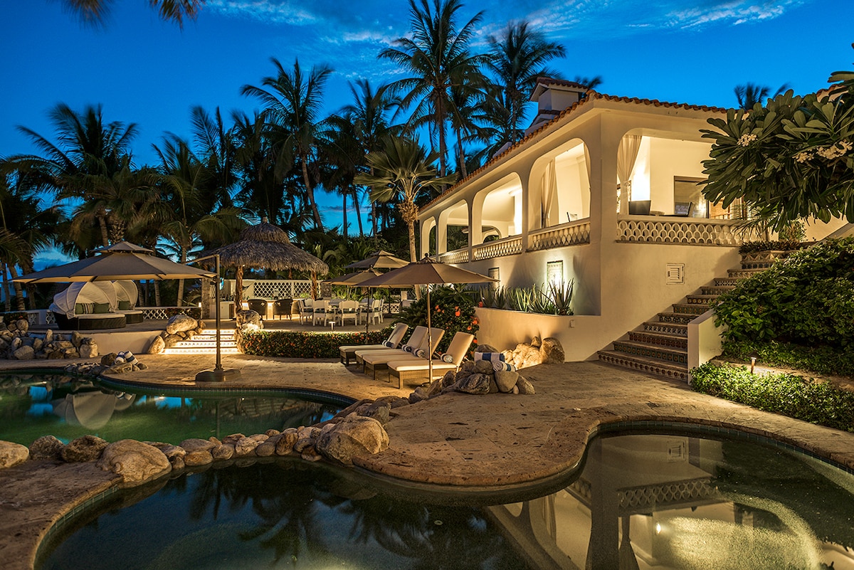 Evening view of the pool, palapa and villa surrounded by palms at Casa Edwards, Palmilla